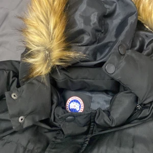Svart dunjacka från Canada Goose - Säljer en svart dunjacka från Canada Goose i storlek XXL. Jackan har en avtagbar huva med snygg pälsdetalj och dragkedja framtill. Perfekt för kalla vinterdagar! 🖤