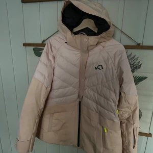 Ljusrosa dunjacka från Kari Traa - Säljer en superfin ljusrosa dunjacka från Kari Traa i storlek L. Jackan har en quiltad design med dragkedja och huva, perfekt för kyliga dagar. Den har också praktiska fickor med neonfärgade detaljer. Perfekt för både vardag och utomhusaktiviteter!