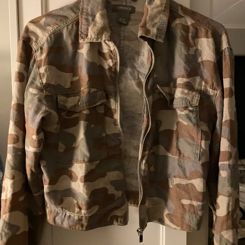 Säljer en cool camouflagejacka från Lindex i storlek XS. Jackan har en dragkedja framtill och praktiska fickor med knappar. Perfekt för en avslappnad stil och passar bra till höst och vår. Den är i bra skick och redo för nya äventyr!. Jackor.