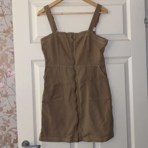 Beige klänning från H&M Divided - Säljer en snygg beige klänning från H&M Divided i storlek L. Klänningen har en dragkedja framtill och breda justerbara axelband. Perfekt för vår och sommar! 👜