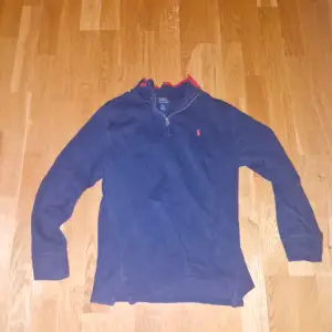 Säljer en snygg mörkblå tröja från Ralph Lauren med röd krage och dragkedja. Perfekt för höst och vinter, den är både stilren och bekväm. Tröjan har långa ärmar och det klassiska Ralph Lauren-märket på bröstet. Passar perfekt för en casual look!