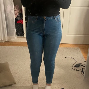 Blå skinny jeans - Säljer ett par snygga blå skinny jeans i mycket bra skick. De är högmidjade och sitter riktigt bra, perfekt för både vardag och fest. Jeansen har en klassisk femficksdesign och stängs med dragkedja och knapp. Superbekväma och stretchiga, så de passar till det mesta i garderoben!