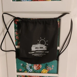 Regn tät gympa påse från Båg Base - Säljer en svart gympapåse från BagBase i nytt skick. Den har ett tryck med texten 'HSB Skåne Sommarkollo i Mjöhult' och är perfekt för träning eller vardagsbruk. Påsen har dragsko för enkel öppning och stängning. Perfekt för att bära med sig det nödvändigaste! 🖤
