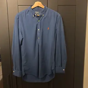 Säljer en snygg blå skjorta från Polo Ralph Lauren i slim fit. Skjortan har långa ärmar och knappar fram. Den är broderad med det klassiska logotypen i orange på bröstet. Perfekt för både vardag och fest! 💙