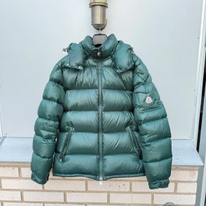 Grön Moncler Maya - Säljer en grön Moncler Maya i gott skick. Fullt fungerande QR samt NFC. Finns några svagt synliga fläckar (se bild 5) inget man tänker på, kan även gå att tvätta bort, har inte provat. Storlek 4, om du är osäker på storlek så uppskattar jag jackan till en Large. Vid frågor eller fler bilder bara skriv! :)