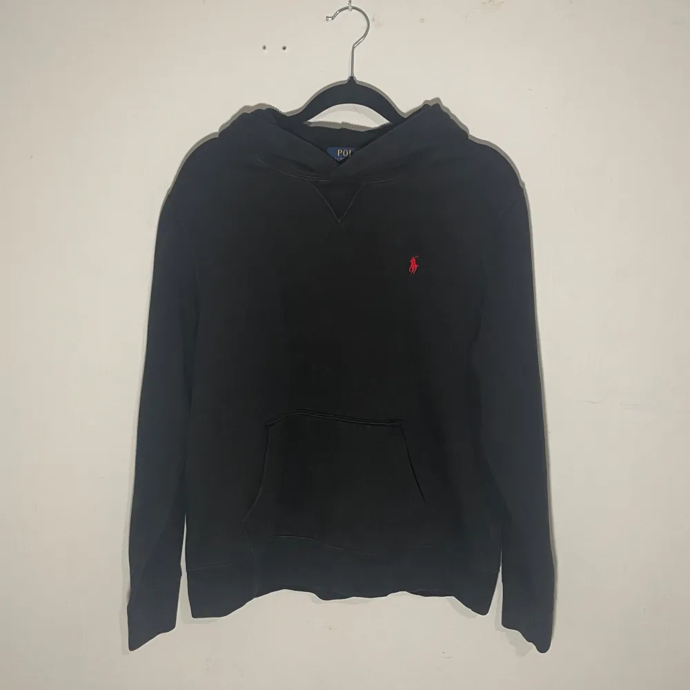 Säljer en klassisk svart hoodie från Ralph Lauren i storlek barn XL vilket motsvarar herr XS. Den har en liten röd logga på bröstet och en stor ficka framtill. Perfekt för höst och vinter, och den är i mycket bra skick. Superbekväm och stilren, passar till allt! 🖤. Hoodies.