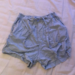 Högmidjade shorts med knytdetalj - Blå högmidjade shorts i materialet lyocell från H&M. De är väldigt mjuka och har snören framtill som man kan knyta. De är använda några gånger men har inga defekter.🩵