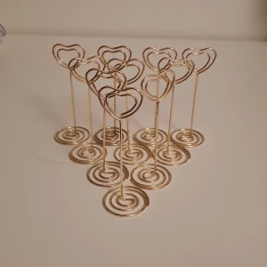 Guldiga hjärtformade kortställ - Säljer ett set med guldiga kortställ i form av hjärtan. Perfekta för att hålla upp kort eller små skyltar vid speciella tillfällen som bröllop eller fester. De har en stabil spiralformad bas som gör att de står stadigt. Superfina och romantiska detaljer för att göra din dukning extra speciell! 💖