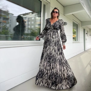 Mönstrad långklänning - Säljer en superfin långklänning med ett unikt mönster i svart och beige. Klänningen har långa ärmar och en v-ringad design som ger en elegant look. Perfekt för höst och vår, och funkar lika bra till fest som till vardags. Materialet känns mjukt och bekvämt. Passa på att fynda denna stiliga klänning!Helt ny