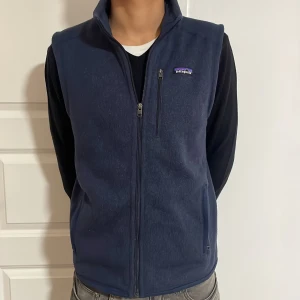 Mörkblå fleeceväst från Patagonia - Säljer en snygg mörkblå fleeceväst från Patagonia i mycket bra skick. Västen har en dragkedja framtill och praktiska fickor. Perfekt för lager-på-lager under höst och vår. Den är både stilren och funktionell, idealisk för både vardag och utomhusaktiviteter. Modellen är 180. Priset ej hugget i sten och hör av er vid frågor funderingar!