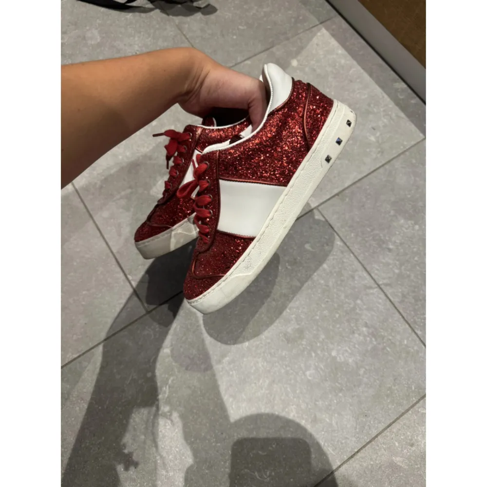 Säljer ett par supercoola röda glittriga sneakers från Valentino! De har en vit rand på sidan och snygga nitar på sulan. Perfekta för att sticka ut på festen eller bara liva upp vardagslooken, man får sjukt mycket komplimanger! Skorna är i bra skick och har en bekväm passform. Med dessa ingår dustbag, låda och äktetsbevis (kort)! Dem är som nya utöver en nit som åkt av, köpt här på Plick och var tyvärr lite för små för mig som har 38 i vanliga fall. Så passar en 36/37🫶🏼. Skor.