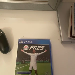 PlayStation 4 med FC25 spel 2 - Säljer en PlayStation 4 med spelet FC25. Konsolen är svart och kommer med en handkontroll. Perfekt för fotbollsfans som vill spela det senaste spelet i serien. Allt är i bra skick och redo för nya äventyr på planen!