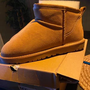 Bruna UGG boots i mocka - Säljer ett par snygga bruna UGG boots i mjuk mocka. Perfekta för höst och vinter med sin varma och bekväma design. De har en robust sula som ger bra grepp och är i nytt skick. Passar perfekt för att hålla fötterna varma och stiliga under kalla dagar.