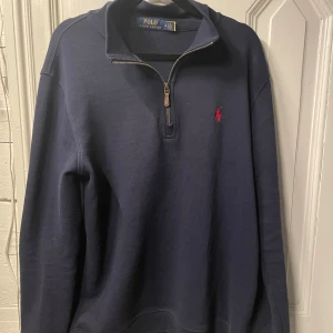 Mörkblå tröja från Polo Ralph Lauren - Säljer en snygg mörkblå tröja från Polo Ralph Lauren i storlek M. Tröjan har en dragkedja vid halsen och det klassiska röda logotypbroderiet på bröstet. Perfekt för både vardag och lite finare tillfällen. Passar bra till höst och vår!