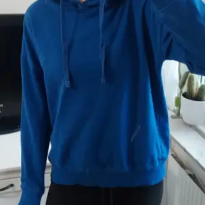 Säljer en snygg blå hoodie i bra skick. Den har en klassisk design med dragsko i huvan och ribbade muddar vid ärmslut och nederkant. Perfekt för en avslappnad stil eller mysiga dagar hemma. Passar till det mesta och är superbekväm!