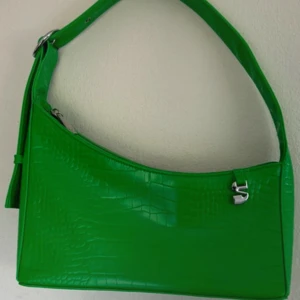 Silfen Grön axelväska med krokodilmönster - Snygg grön axelväska i syntetmaterial med krokodilmönster. Väskan har en dragkedja upptill och en justerbar axelrem. Perfekt för att ge en färgklick till din outfit!