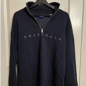 Half-zip mörkblå “originals” stl L - Mörkblå half-zip från jack & jones med “Originals tryck” Half-zipen är ny i skick och är aldrig använd. Den bär stl L men passar storlek M lika bra.