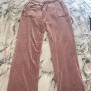 Rosa mjukisbyxor från Juicy Couture - Säljer ett par supermysiga rosa mjukisbyxor från Juicy Couture i storlek L. Byxorna är gjorda av mjuk polyester och elastan, vilket gör dem både bekväma och stretchiga. De har en loose passform med fickor fram och bak, samt en snygg dragsko i midjan. Perfekta för en chill dag hemma eller en avslappnad utflykt! Tyvärr lite smutsiga vid fötterna men inget som syns tydligt. (Pris kan diskuteras)