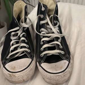 Svarta Converse All Star sneakers - Säljer ett par klassiska svarta Converse All Star sneakers i bra skick. De har den ikoniska vita sulan och snörning, med det välkända logotypmärket på sidan. Perfekta för vardagsbruk och ger en cool, avslappnad stil.