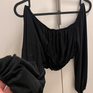 Svart offshoulder topp från NLY One - Snygg svart offshoulder topp från NLY One i storlek L. Toppen har långa ärmar och en elastisk kant som ger en bekväm passform. Materialet är mjukt och stretchigt.