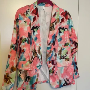 Färgglad kavaj i blommigt mönster - Säljer en superfin kavaj i storlek S med ett färgglatt blommigt mönster. Perfekt för att liva upp vilken outfit som helst! Kavajen har långa ärmar och en normal passform. Den är idealisk för  både  vardags och fest. Helt ny🌸