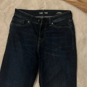 Mörkblå jeans - Säljer ett par mörkblå jeans i mycket bra skick. De har en klassisk femficksdesign med knapp och dragkedja framtill. Perfekta för både vardag och fest. Passformen är slim och de är tillverkade i ett bekvämt denimtyg.