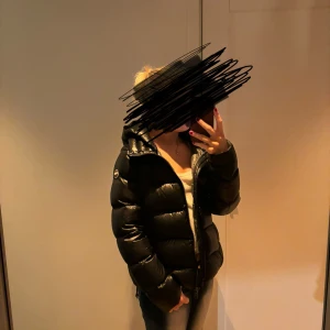 Svart glansig colmarjacka  - Säljer en snygg och varm svart glansig colmar  dunjacka med huva. Perfekt för kalla vinterdagar. Jackan har en dragkedja framtill och är långärmad. Det är bara att höra av sig vid intresse och frågor!!