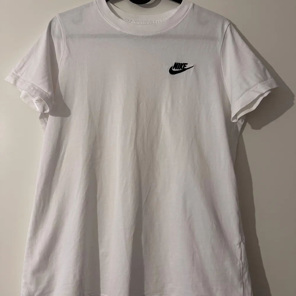 Säljer en klassisk vit t-shirt från Nike i bomull. Den har en liten svart Nike-logga på bröstet och är i mycket bra skick. Perfekt för vardagsbruk eller träning. Storleken är dam M och den har en normal passform.. T-shirts.