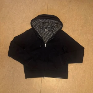 Dior Zip hoodie - Säljer en snygg marinblå zip hoodie från Dior i mycket bra skick. Storlek S men passar M. Den har en dragkedja framtill och ett mönstrat foder i huvan. Perfekt för höst och vinter, med långa ärmar och en bekväm passform. Ett måste för garderoben! Kvitto finns. Tveka inte på att skriva ifall du har några frågor! MVH Darin 