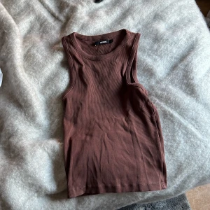 Brun ribbad linnetopp från Bik Bok - Säljer en snygg brun ribbad linnetopp från Bik Bok i storlek M. Perfekt för sommardagar eller som ett lager under en jacka. Toppen är ärmlös och har en tight passform som framhäver figuren. Superbekväm och stilren!