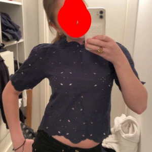 Mörkblå blus med broderade detaljer - Säljer en söt mörkblå blus med korta ärmar och fina broderade detaljer. Blusen har en lätt croppad passform och en elegant halsringning. Perfekt för både vardag och fest!