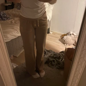Juicy couture Beige mjukisbyxor - Säljer ett par superbekväma beige juicy couture mjukisbyxor. De har en loose passform och är perfekta för mysiga hemmakvällar. Byxorna har snörning i midjan för justerbar passform och är tillverkade i mjukt material. Perfekta för höst och vinter!
