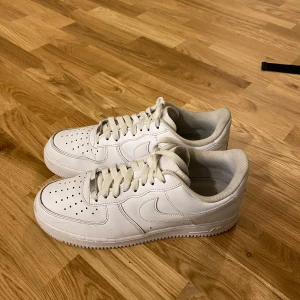 Vita Nike Air Force sneakers - Säljer ett par klassiska vita Nike Air Force sneakers i bra skick. De har en stilren design med snörning och är perfekta för både vardag och fest. Skorna är i skinn och har en bekväm passform. Perfekta för alla säsonger!