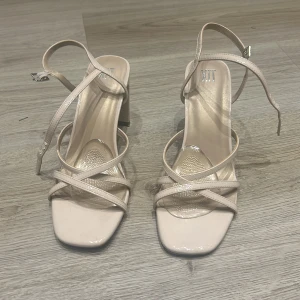 Beige sandaler med klack - Snygga beige sandaler med klack och smala remmar som korsar över foten. De har en fyrkantig tå och justerbara spännen för perfekt passform. Perfekta för sommarens fester eller en utekväll. Stilrena och eleganta!