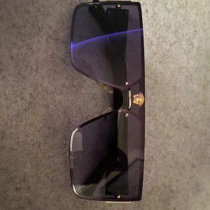 Svarta solglasögon med gulddetaljer - Snygga svarta solglasögon med en rektangulär form och coola gulddetaljer på bågarna. Perfekta för att ge en stilren look. De har en bred passform och mörka linser som skyddar mot solen.