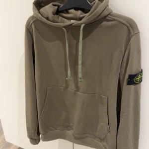 Olivgrön hoodie från Stone Island - Säljer en snygg olivgrön hoodie från Stone Island med klassisk logga på ärmen. Tröjan har en stor ficka framtill och justerbar huva med dragsko. Perfekt för en avslappnad stil.Frakten står köparen för. Storlek L men sitter som M. Använde Max 2 gånger och är i ny skick!!