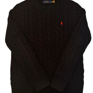 Svart stickad tröja från Ralph Lauren - Säljer en stilren svart stickad tröja från Ralph Lauren med det klassiska röda logotypen broderad på bröstet. Tröjan har en kabelstickad design och långa ärmar, perfekt för kyligare dagar. Passar både till vardags och mer uppklädda tillfällen. Värt att nämna att halsringen är något stor, men absolut inget extremt.                Kontakta gärna vid frågor eller prisförslag!