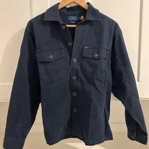 Blå overshirt från Polo Ralph Lauren - Säljer en stilren blå overshirt från Polo Ralph Lauren. Den har knappar framtill och två bröstfickor med knappstängning. Perfekt för lager-på-lager-stil. Klassisk passform och långärmad design.