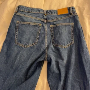 Blå jeans från Monki - Snygga blå jeans från Monki med klassisk femficksdesign och guldfärgade sömmar. De har en rak passform och är perfekta för en avslappnad stil. Jeansen har en knapp och dragkedja framtill.