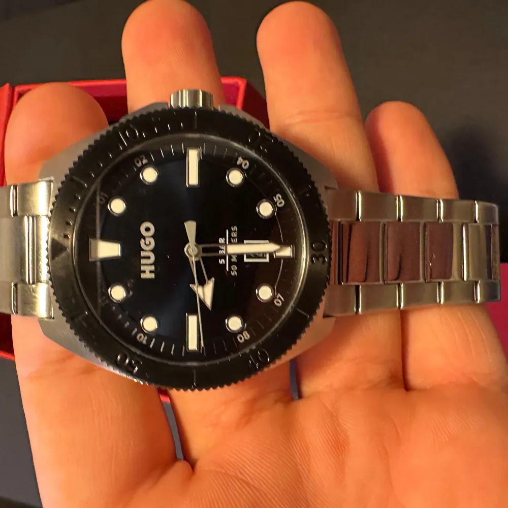 Snygg klocka från Hugo med silverfärgad länk och svart urtavla. Klockan har tydliga markeringar och datumvisning. Perfekt för den stilmedvetna som vill ha en tidlös accessoar.. Asusteet.
