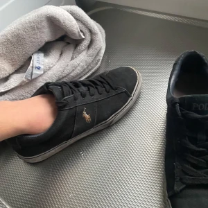 Svarta sneakers från Polo Ralph Lauren - Lite slitiga men går att tvätta så De blir snygga Snygga svarta sneakers från Polo Ralph Lauren med klassisk design. Skorna har en broderad logotyp på sidan och snörning framtill. Perfekta för en avslappnad stil.