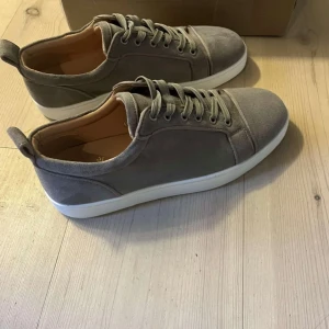 Gråa Christian Louboutin - Snygga grå sneakers från Christian Louboutin med klassisk röd sula. Skorna har snörning och är tillverkade i ett stilrent material som ger en lyxig känsla. Perfekta för den som vill ha en stilren look med en touch av exklusivitet. De är använda. Men superfint skick, lite creasade på hälen. Skriv vid funderingar