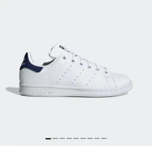Vita Adidas Stan Smith sneakers🩷 - Klassiska vita Adidas Stan Smith sneakers med mörkblå detaljer på hälen. Skorna har en stilren design med perforerade ränder på sidorna och snörning framtill. Perfekta för en avslappnad och trendig look.