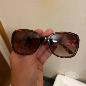 Leopardmönstrade solglasögon från Miki - Snygga solglasögon med leopardmönster och stora fyrkantiga bågar. De har en cool guldig Miki-logga på sidorna som ger en lyxig touch. Perfekta för att sticka ut i mängden!