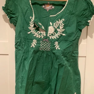 Grön blus från Odd Molly stl 2 (EU38) - Charmig grön blusfrån Odd Molly med vackra broderade detaljer i vitt. Klänningen har korta ärmar med spetskant och en smickrande v-ringning. Perfekt för en bohemisk look.väldigt bra skick