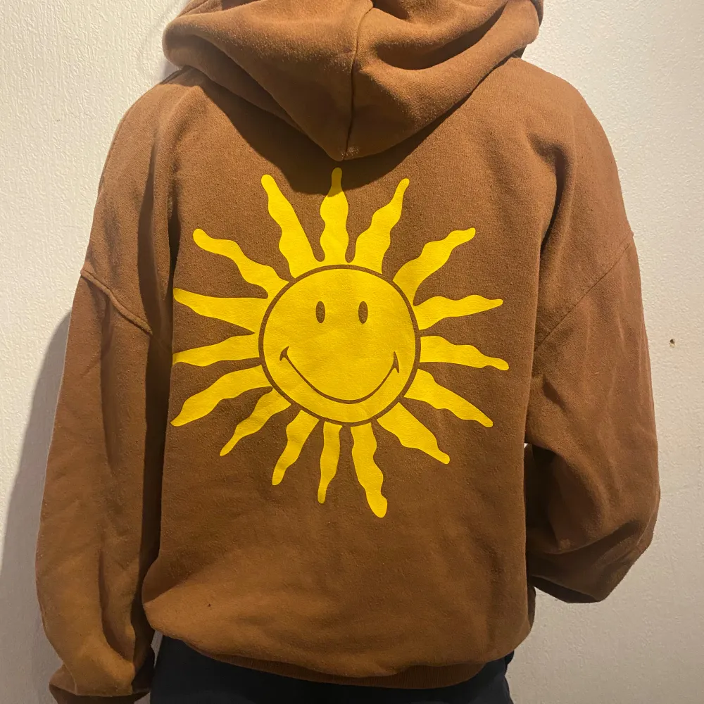 Supermysig brun hoodie med dragkedja. Den har en stor gul sol tryckt på ryggen och en mindre sol på framsidan. Perfekt för höst och vår när det är lite kyligt. Den är långärmad och har en skön luva.. Jackor.