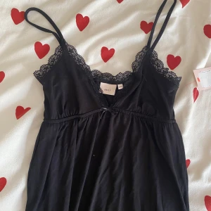 Svart klänning med spetsdetaljer från Nelly - Säljer en superfin svart klänning från Nelly i storlek XXS. Den har tunna axelband och vacker spets runt halsringningen. Materialet känns mjukt och bekvämt mot huden. Helt ny med prislapp, i perfekt skick! 🤍 