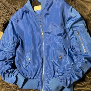 Blå bomberjacka - Snygg blå bomberjacka med dragkedja och fickor med knappar. Sitter lite oversized på mig (storlek S) vilket är jag personligen tycker är supersnyggt. 