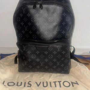 Svart ryggsäck från Louis Vuitton - Snygg svart ryggsäck från Louis Vuitton med det klassiska monogrammönstret. Ryggsäcken har flera dragkedjor och justerbara axelremmar för bekväm användning. Perfekt för att bära dina dagliga nödvändigheter med stil.