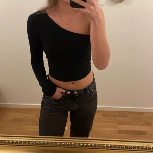 Svart oneshoulder topp - Snygg svart oneshoulder topp med lång ärm. Perfekt för en trendig look. Toppen är croppad och passar utmärkt till både jeans och kjol.